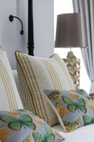 Una cama con almohadas adornadas con un estampado de mariposas y una lámpara geométrica al fondo.