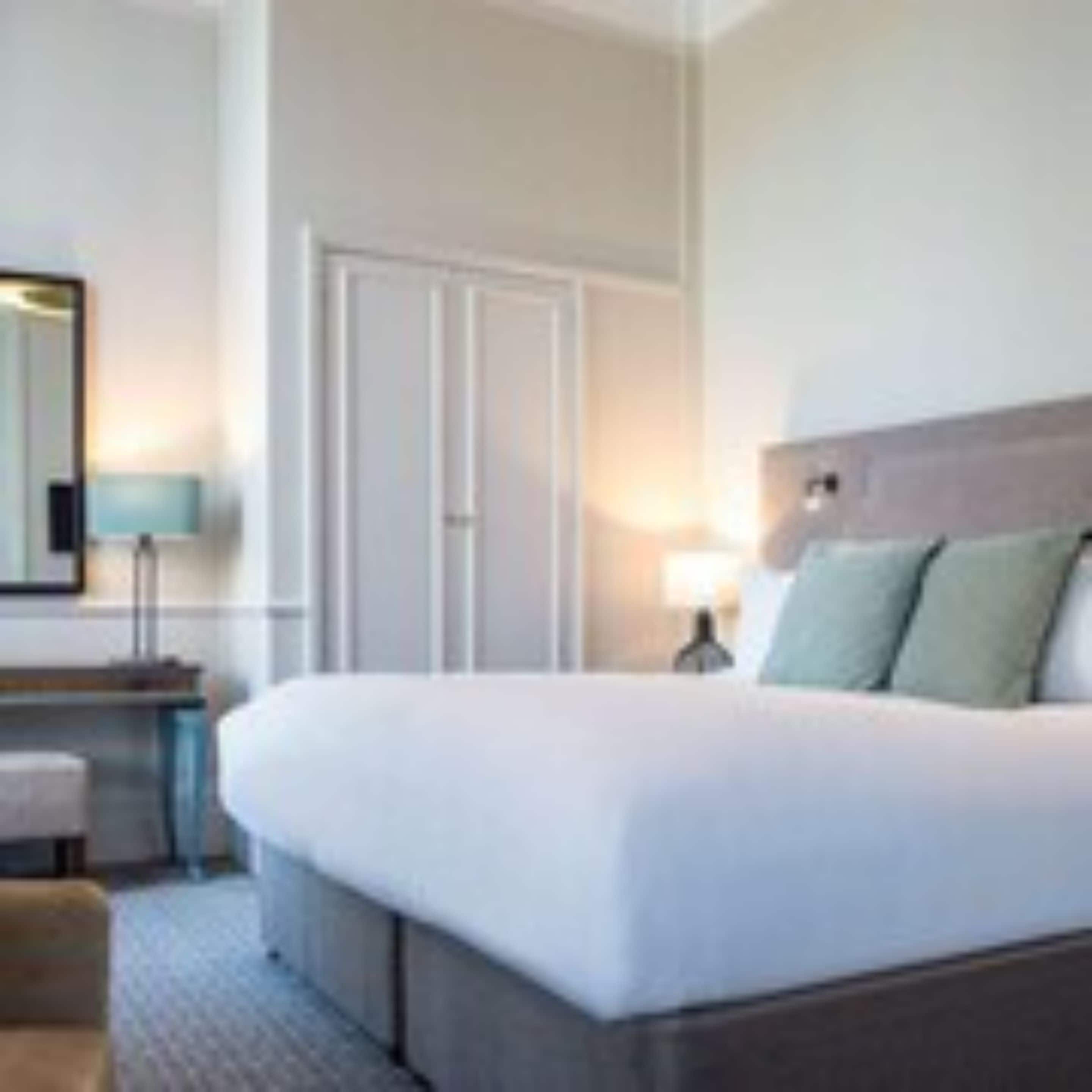Una habitación de hotel con una cama grande, una mesita de noche, una lámpara y una puerta.