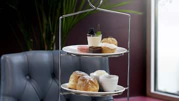 A three-tiered tea service stand with pastries and sandwiches, surrounded by floral teacups and a teapot on a wooden table.