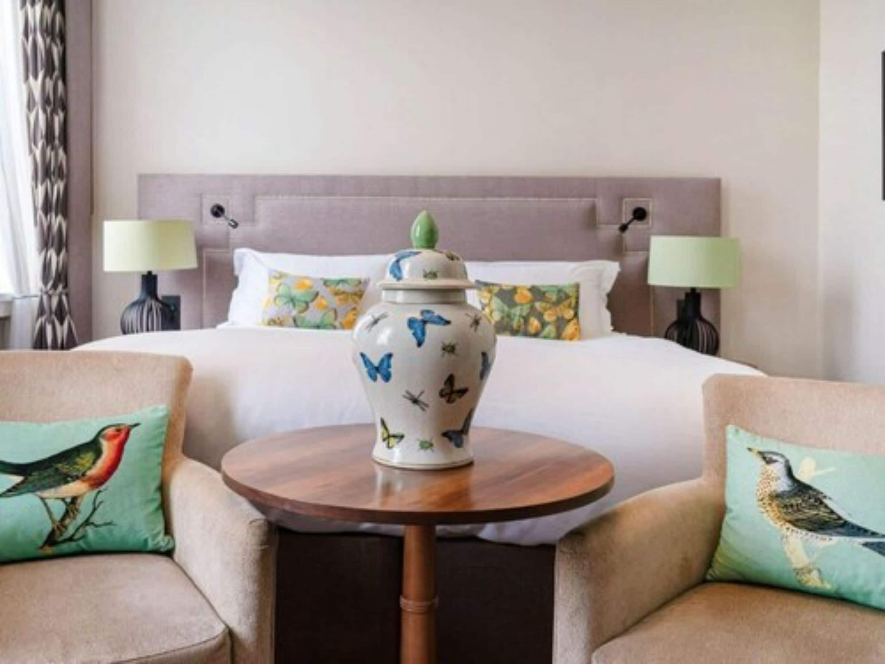 A hotel room with a bed, two chairs, a small round table, and a decorative vase.