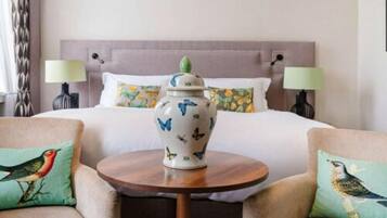 A hotel room with a bed, two chairs, a small round table, and a decorative vase.