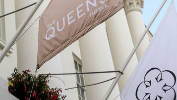 Eine Flagge mit dem Schriftzug "The Queens Hotel", weißen Säulen und blauem Himmel.