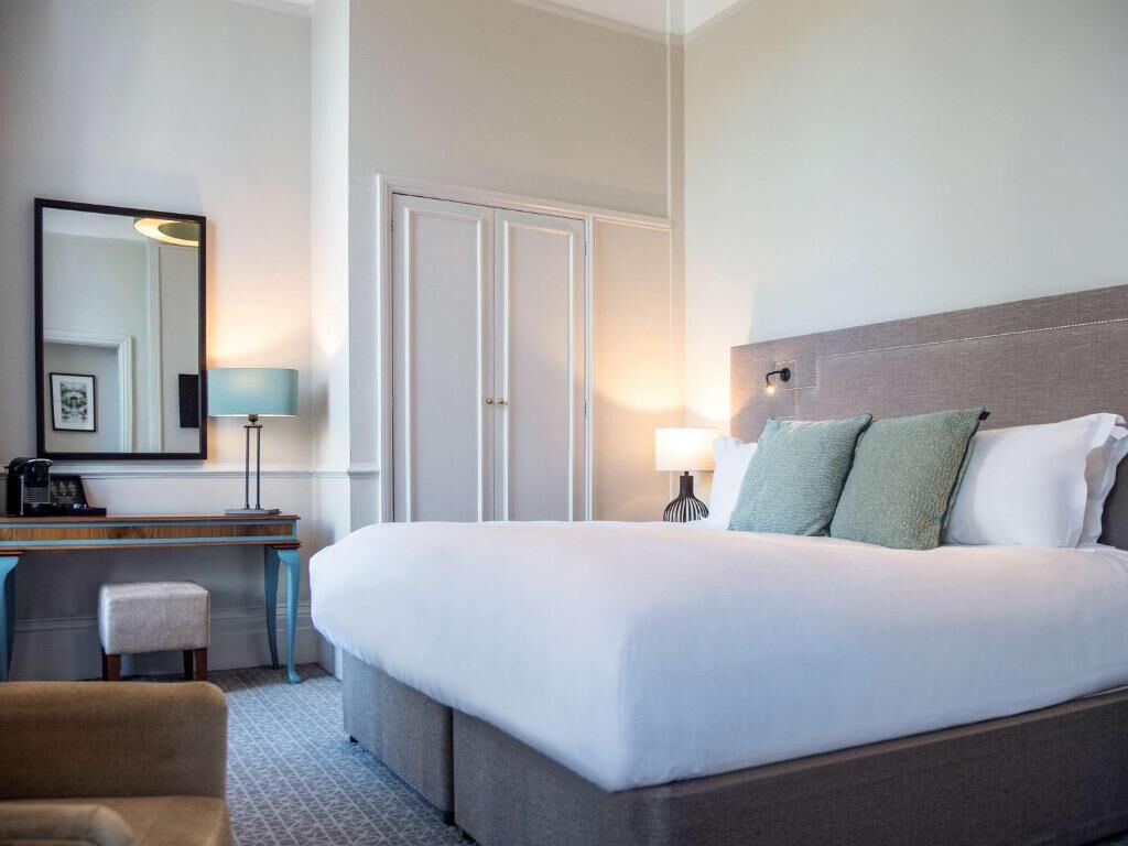 A hotel room with a bed, a desk, a chair, a lamp, and a wardrobe.