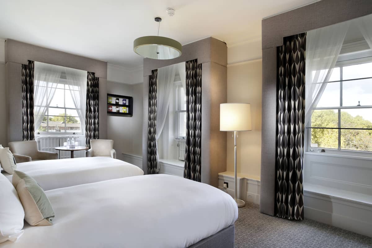 A hotel room with two beds, a desk, a chair, a TV, and a window with curtains.