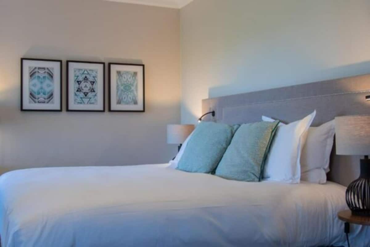 A neatly made bed with pillows, a bedside lamp, and three framed artworks on the wall.