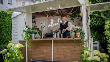 Un pequeño bar al aire libre con mostrador de madera, un letrero de neón y varias plantas a su alrededor.