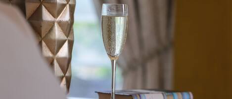 A clear glass of champagne on a wooden table with books, set against a geometric-patterned curtain.