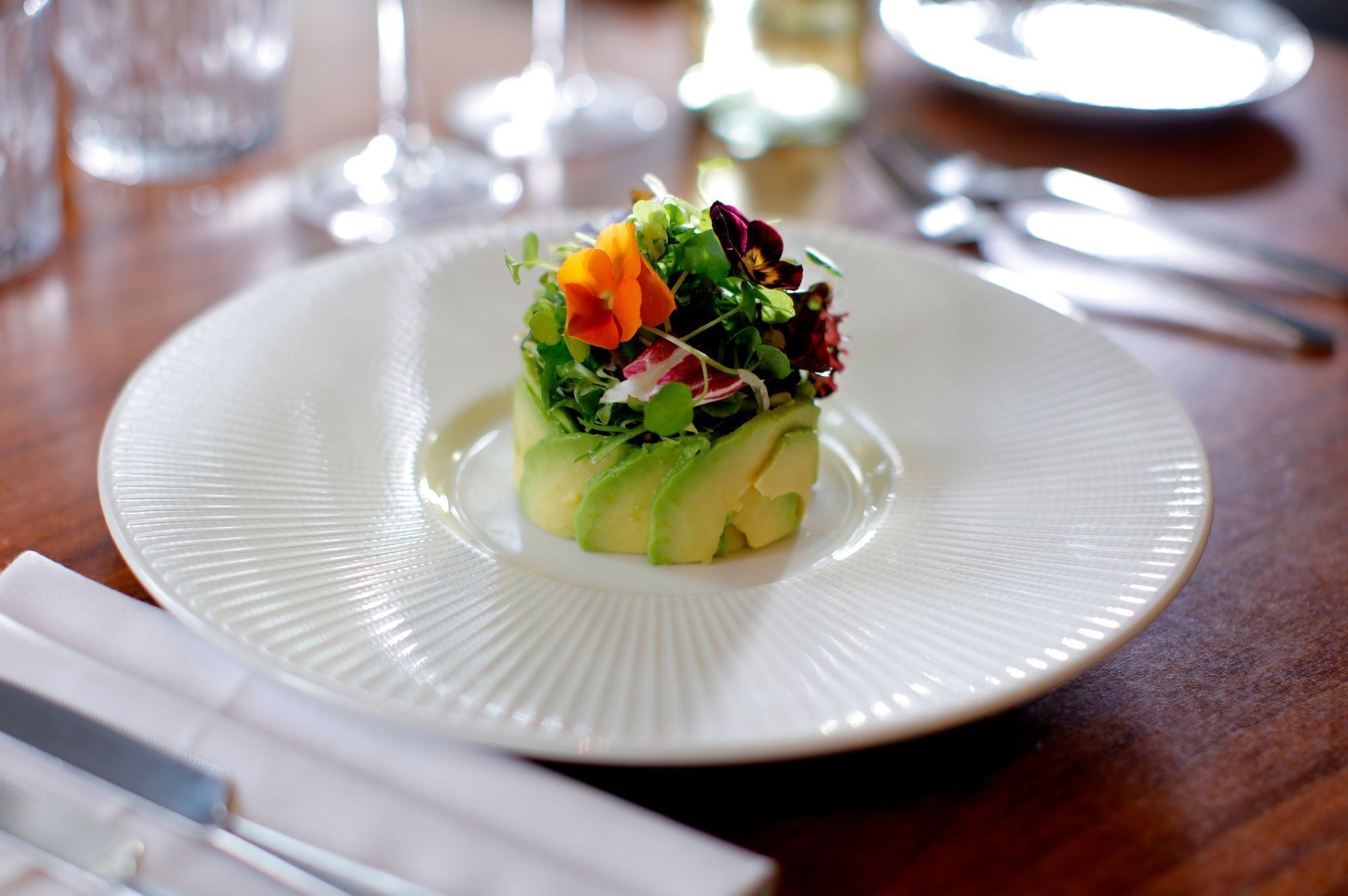A white plate with a salad on a wooden table.