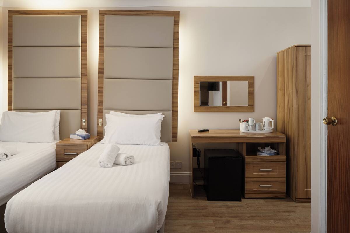 A hotel room with two beds, a wooden headboard, a desk with a mirror, and a wardrobe.