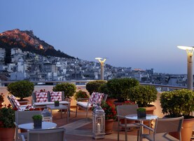 Μια ταράτσα με υπαίθριο χώρο για καθιστικό, γλάστρες με φυτά και θέα στην πόλη, με ένα βουνό να διακρίνεται στο βάθος.