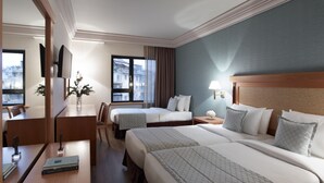 Quarto de hotel com duas camas, uma escrivaninha com cadeira, televisão, janela com vista para edifícios e abajur.