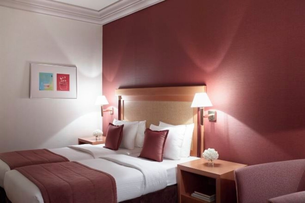 A hotel room with two beds, a nightstand with a lamp, and a small table with a decorative item.