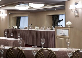 Sala de conferências com uma mesa comprida, microfones e um pódio com a placa do nome do hotel.