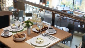 Uma mesa de jantar posta com pratos, copos e talheres, com vista para a rua.