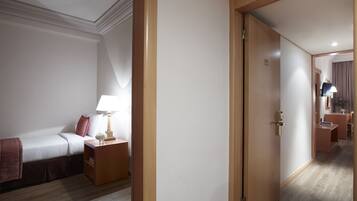 A hotel room with a bed, bedside table, lamp, and a door leading to another room.