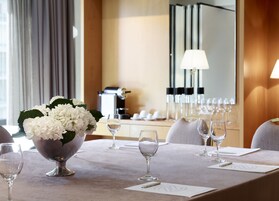 Habitación de hotel con una mesa de comedor dispuesta para una comida, una cafetera y un espejo que refleja la decoración de la habitación.
