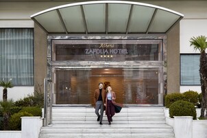 Ateenan Zafolia -hotellin modernisti suunniteltu sisäänkäynti, jossa on lasijulkisivu ja kaareva katto.