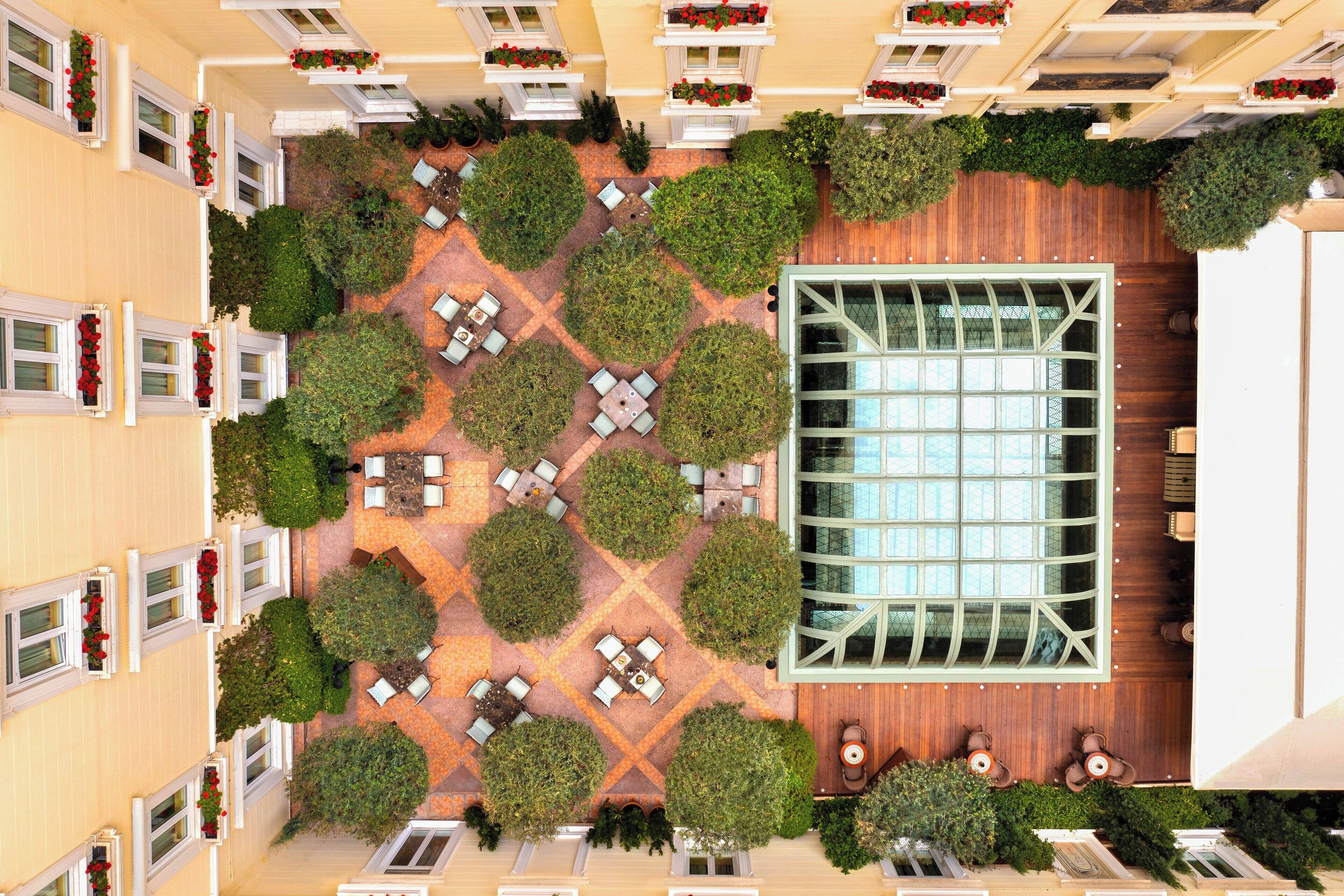Vista aérea de un patio de hotel con una sala central de vidrio, rodeado de zonas de estar ordenadas y follaje.