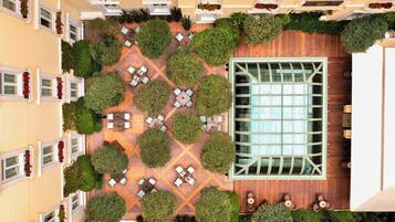 Vista aérea de un patio de hotel con una sala central de vidrio, rodeado de zonas de estar ordenadas y follaje.