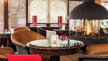 A cozy lounge area with leather chairs, a round table, a large globe artwork, and a central fire feature.