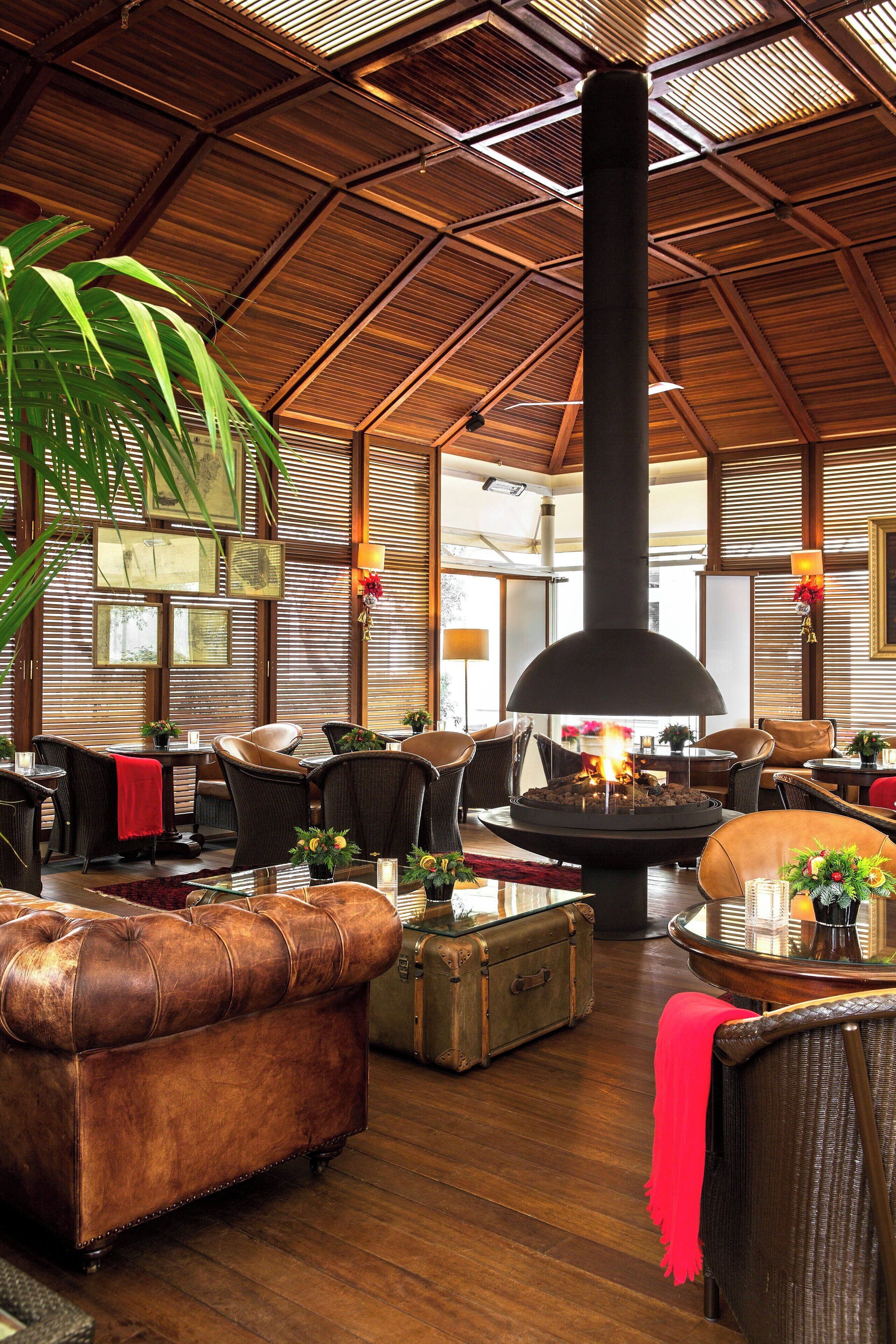 Un salón espacioso con techo alto, chimenea de leña en el centro, asientos de cuero y paredes de madera.