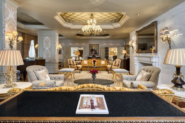 Un salon luxueux, agrémenté d’un grand lustre, de meubles élégants et d’une table basse centrale sur laquelle repose un magazine.