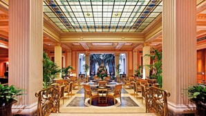 Un amplio vestíbulo con una mesa redonda central, flanqueado por columnas y plantas en macetas.