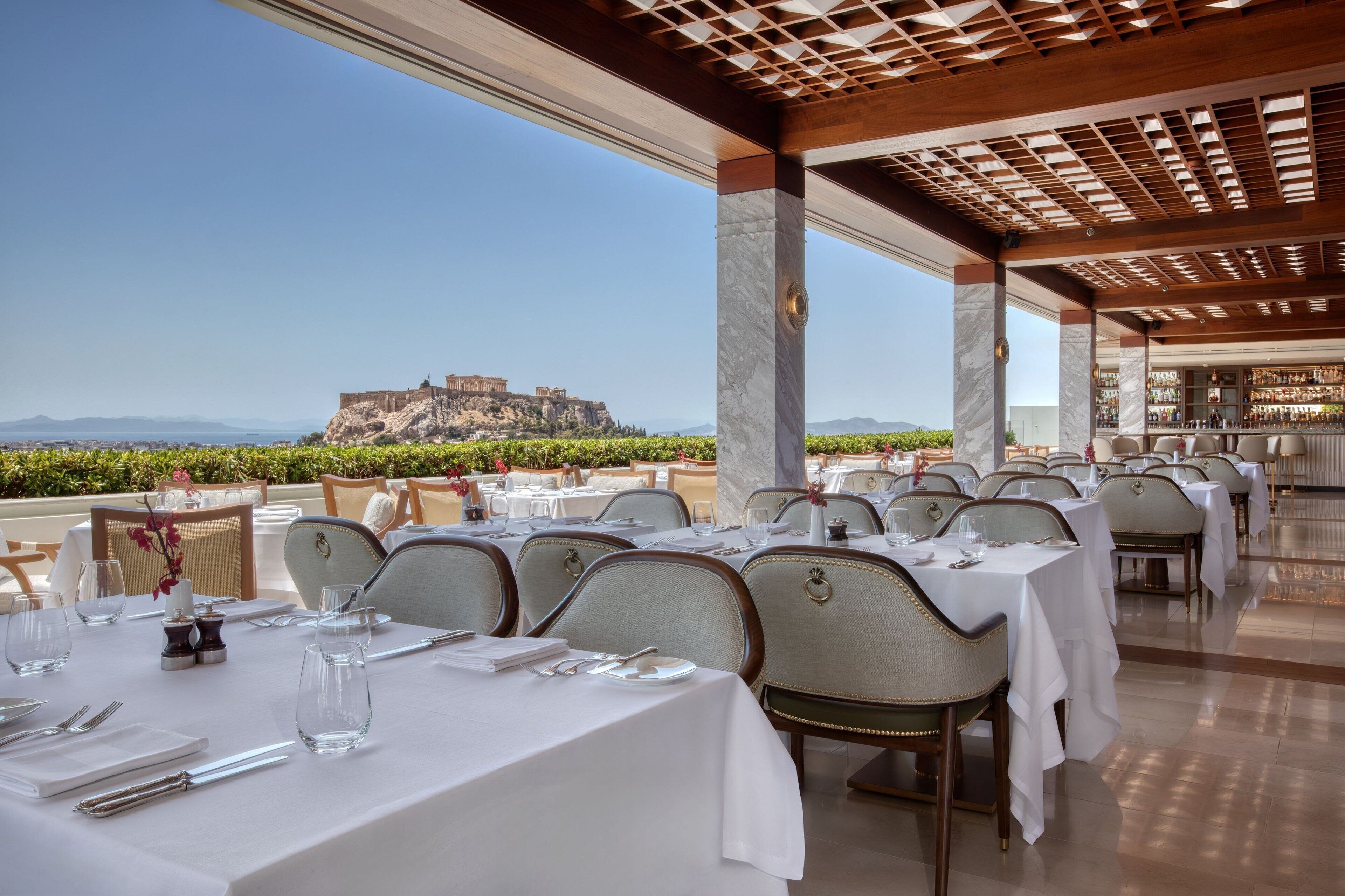 A restaurant with tables set for dining, a view of a historic building, and a clear sky.