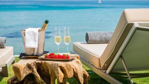 A beachside lounge with a wooden table, a bottle of champagne, two glasses, and a plate of strawberries.