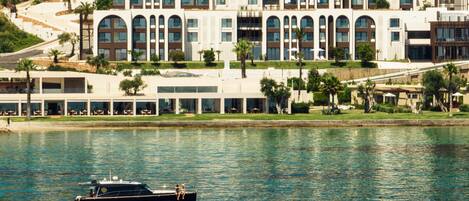A waterfront hotel with a modern architectural design, featuring multiple balconies and large windows.