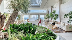 A spacious indoor area with a large tree, seating arrangements, and a piano. - Domes Miramare, a Luxury Collection Resort, Corfu - Adults Only (Corfu)