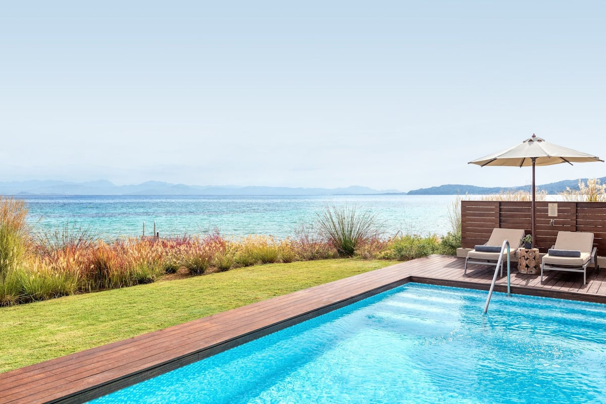 A swimming pool with a wooden deck, two lounge chairs, and an umbrella.