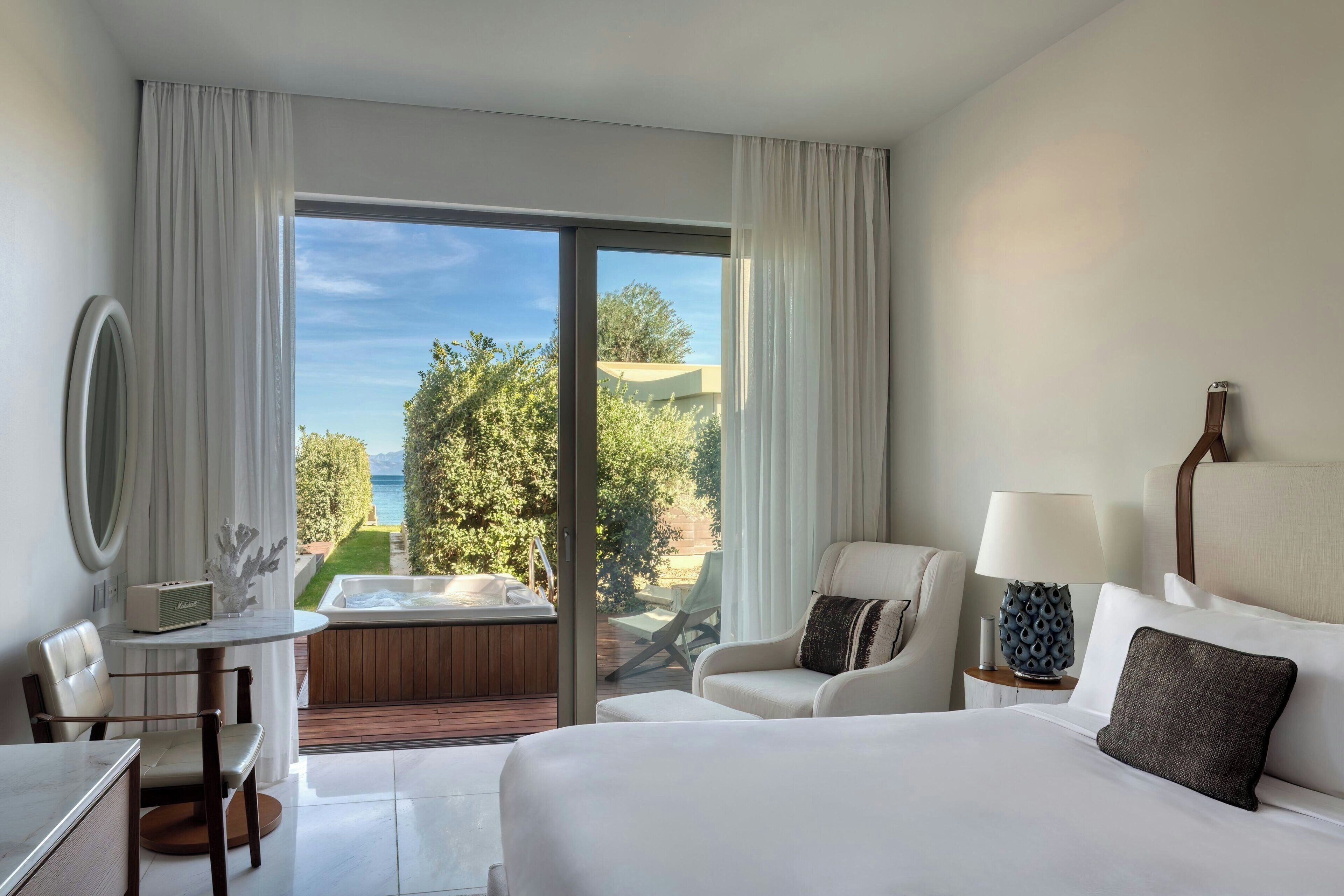 Habitación de hotel con una cama grande, un escritorio con silla, una mesita, un sofá, una lámpara y vistas al exterior.