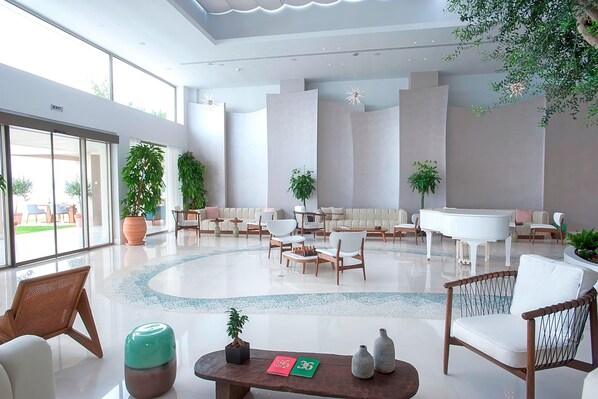 A spacious lobby with a grand piano, comfortable seating, and large windows offering a view of the outdoors.