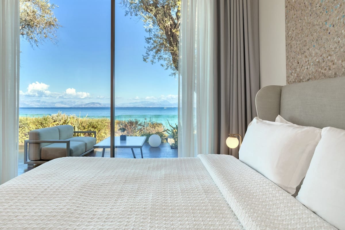 A bedroom with a large bed, a view of the sea, a sofa, and a table.
