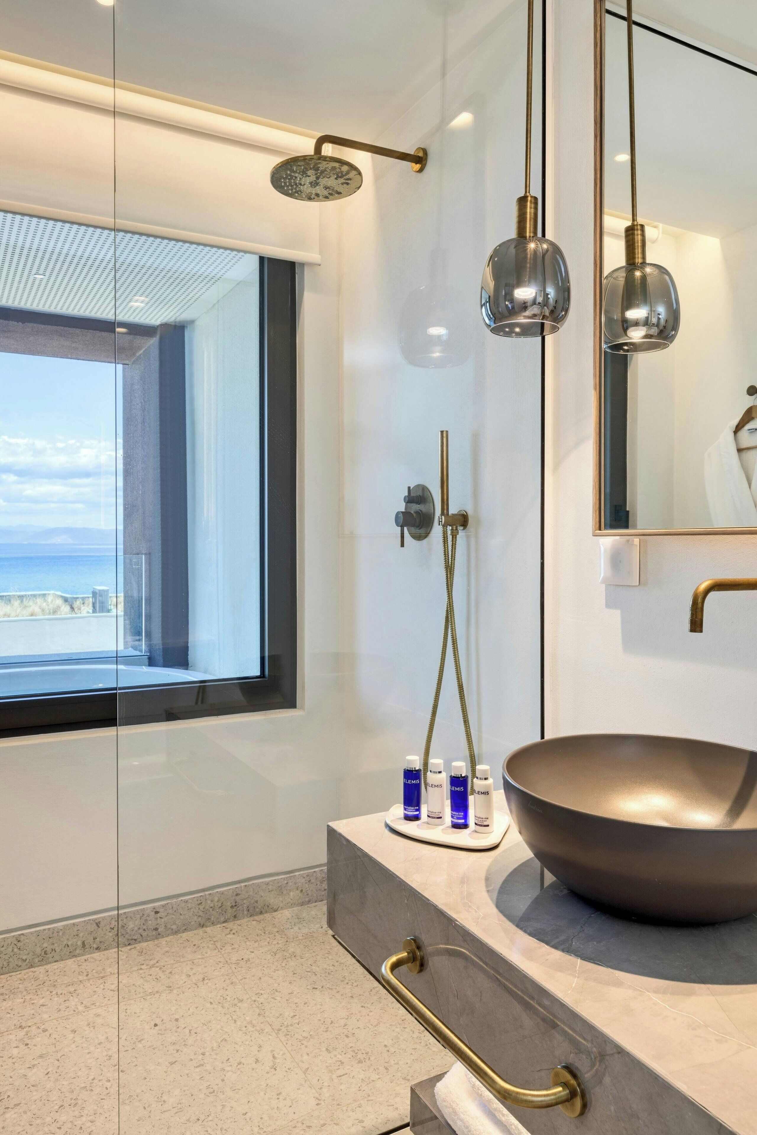 A modern bathroom with a large window, a round sink, and a showerhead.