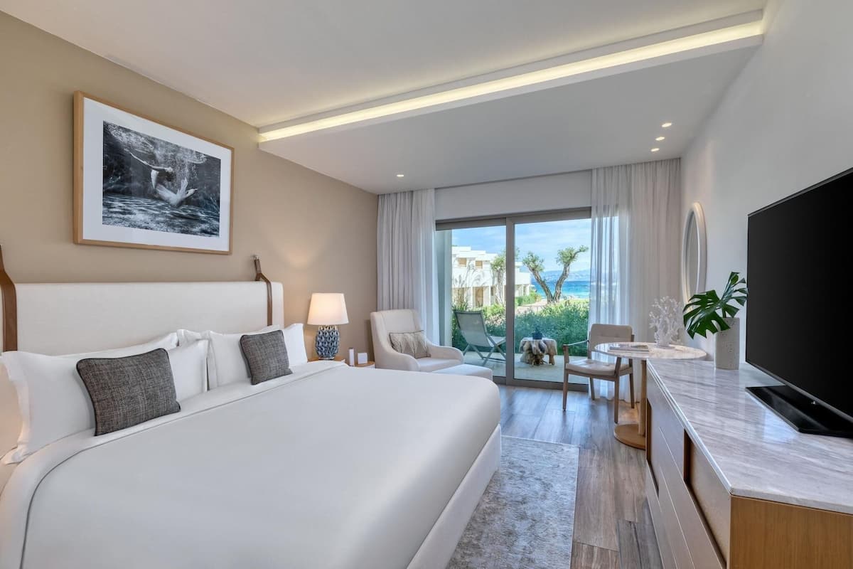 A hotel room with a large bed, a television, a desk, and a view of the ocean.