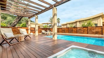 Eine Holzterrasse mit Whirlpool, Liegestühlen, Schwimmbad und einer Pergola.