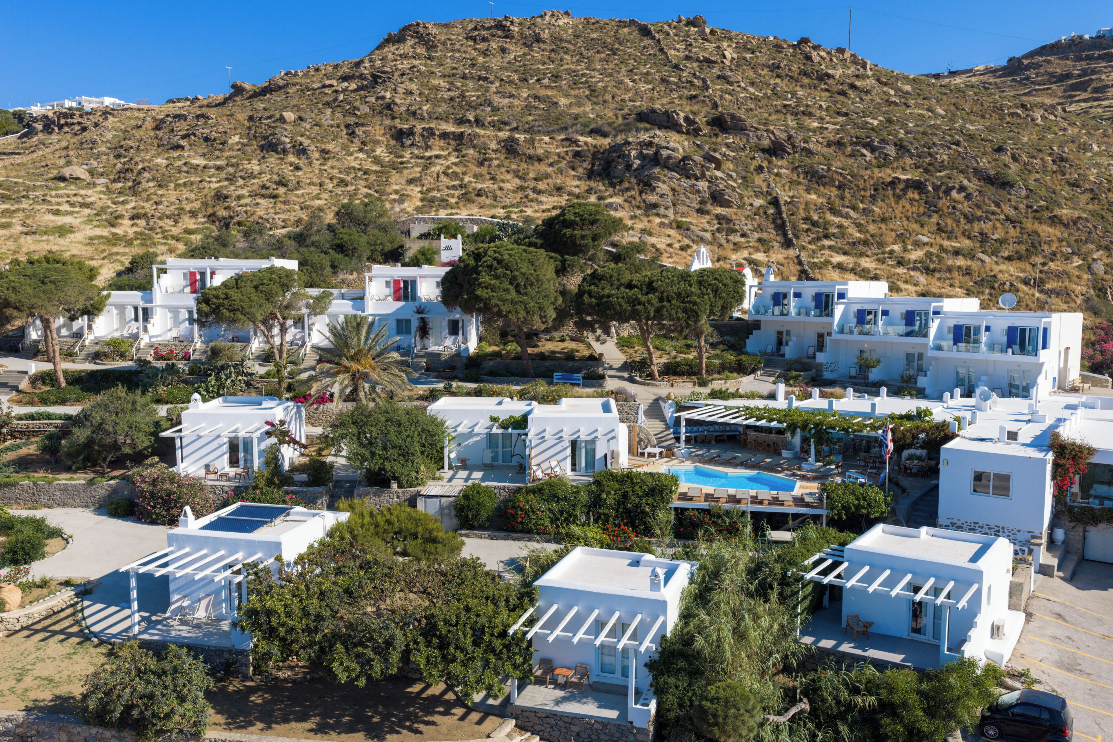 A coastal village with white buildings, a swimming pool, and a hillside backdrop.