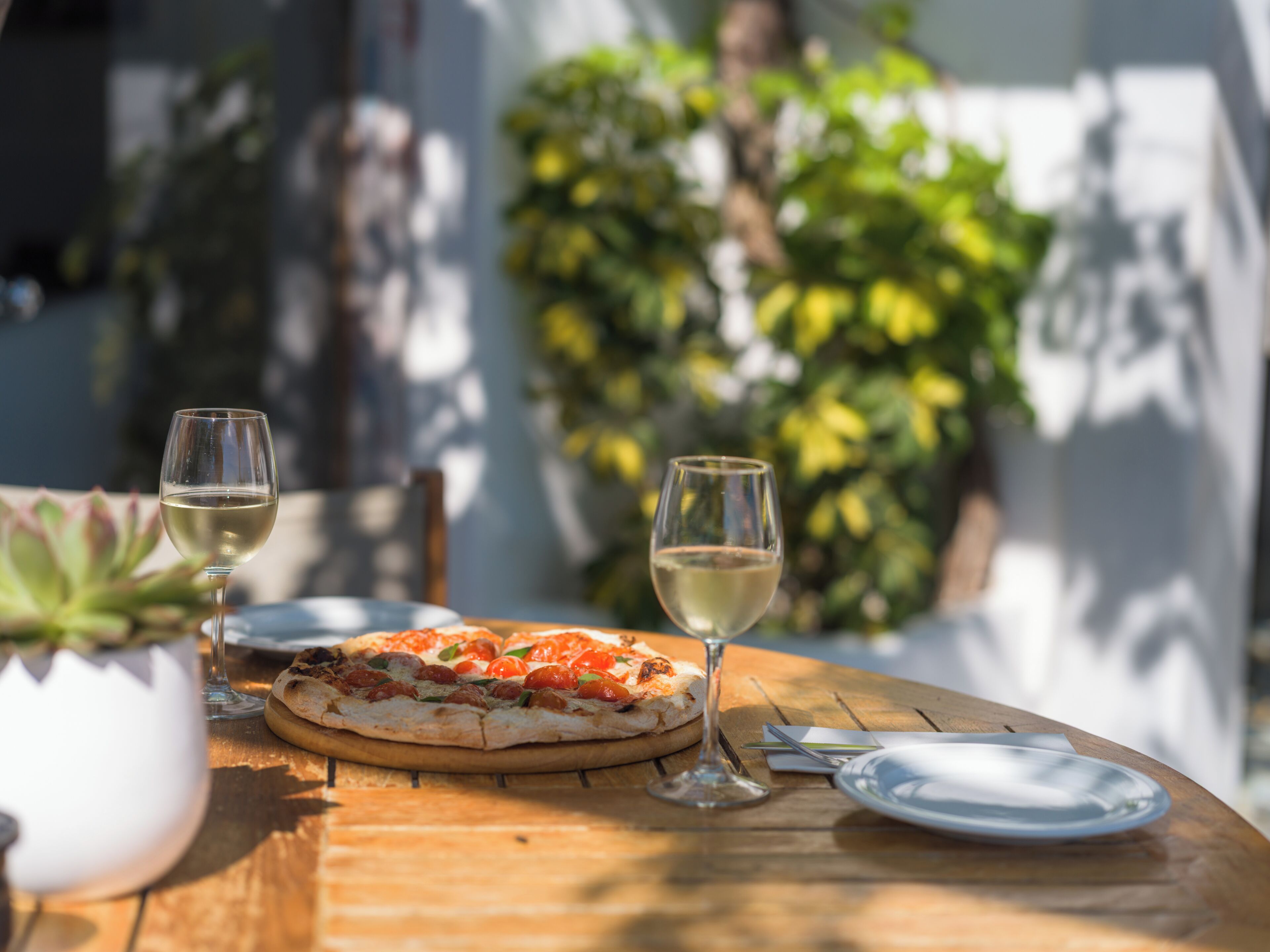 A wooden table with a pizza, two wine glasses, and a plate.