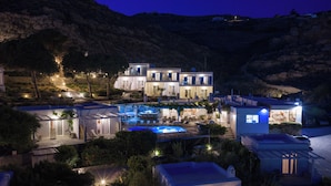 Un hotel de varios pisos con piscina, mobiliario exterior y vistas a una zona montañosa.