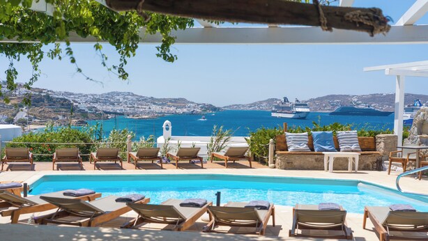 Un área junto a la piscina con sillones de descanso, vista al mar y un crucero a lo lejos.