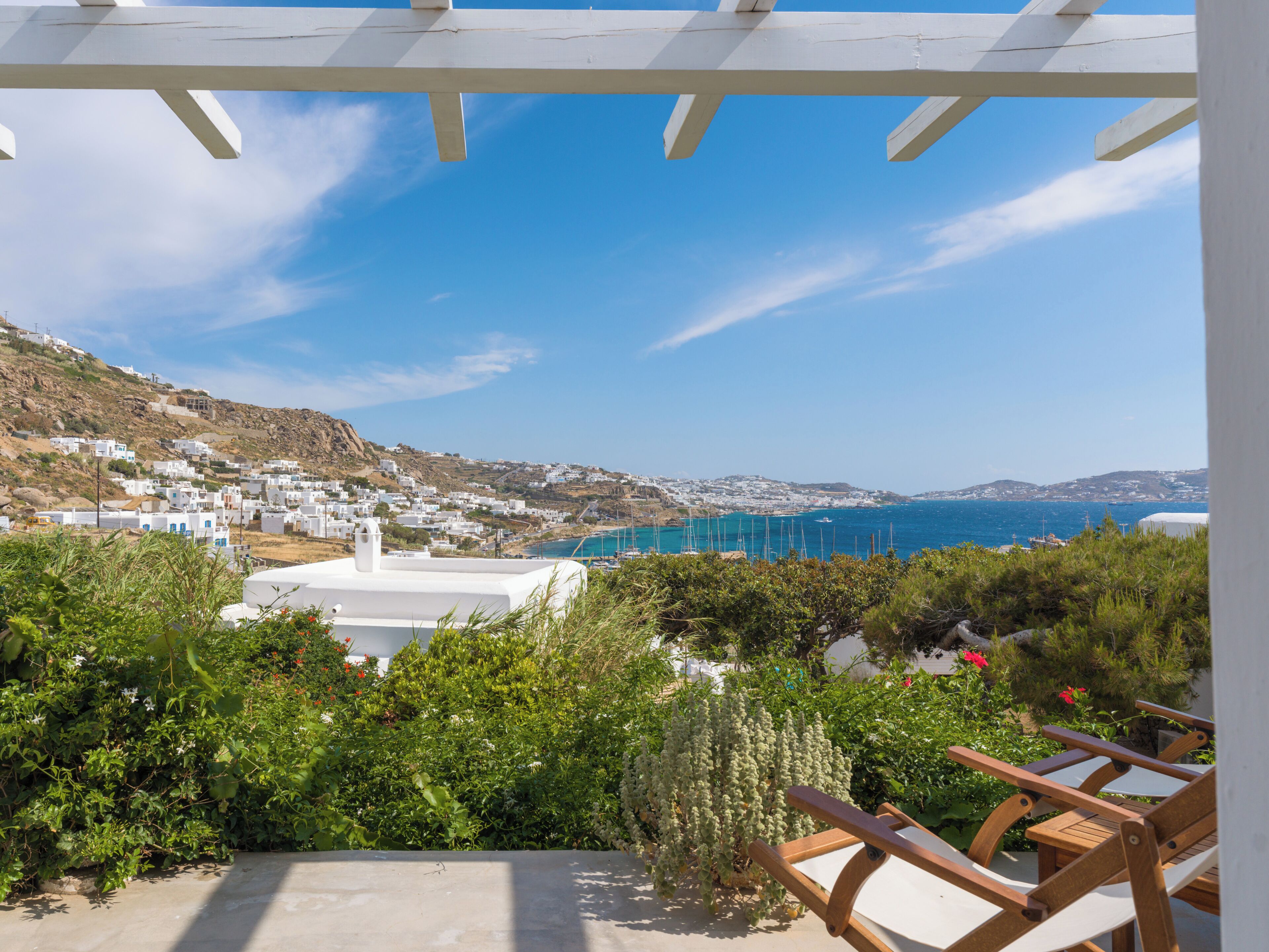 A coastal view with white buildings, a clear sky, and a wooden pergola.