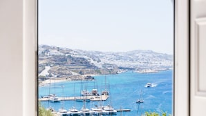 Un puerto costero con barcos amarrados, una vista despejada del mar y un pueblo distante en la colina.