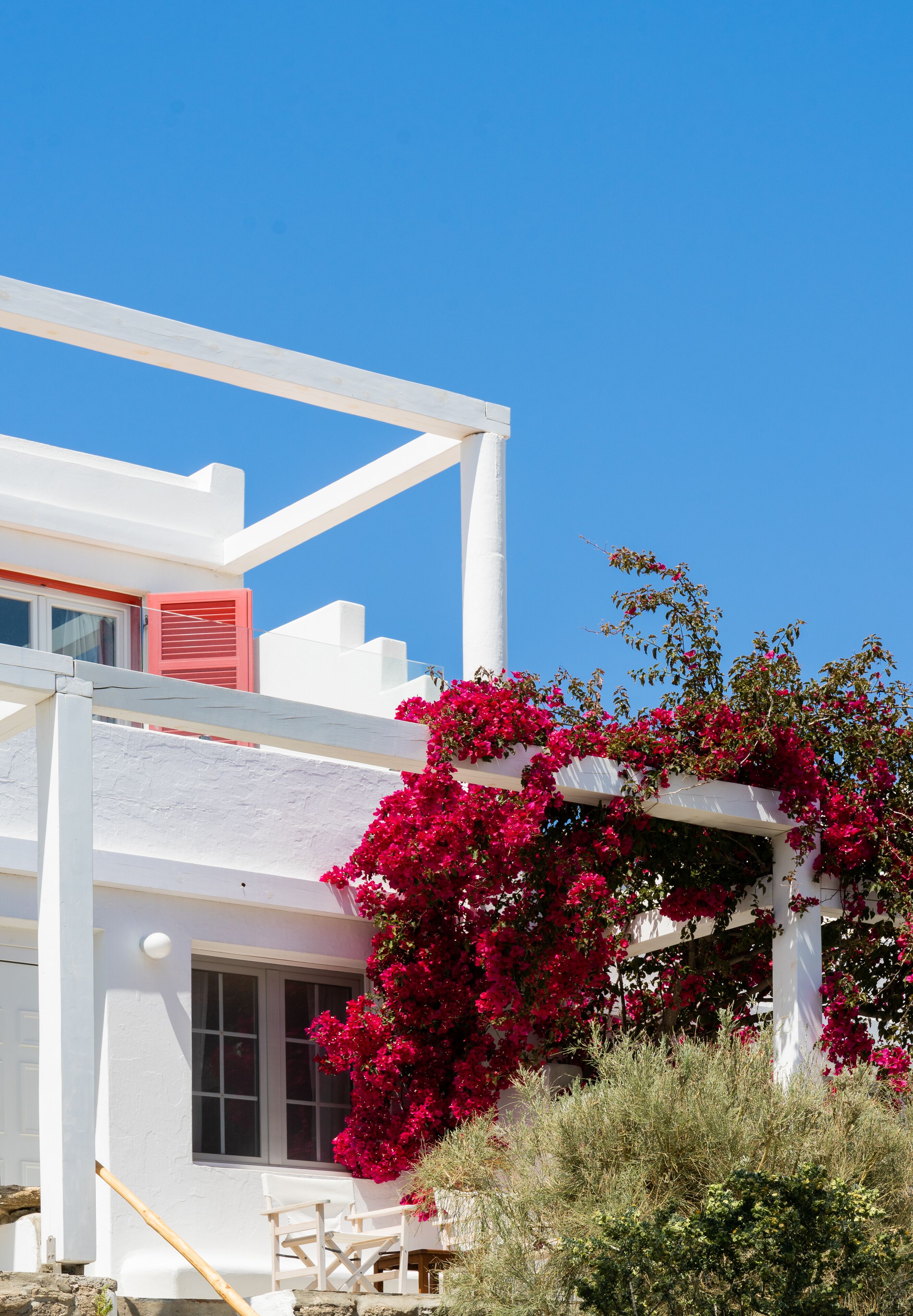 A white building with a balcony, red shutters, and pink bougainvillea flowers.