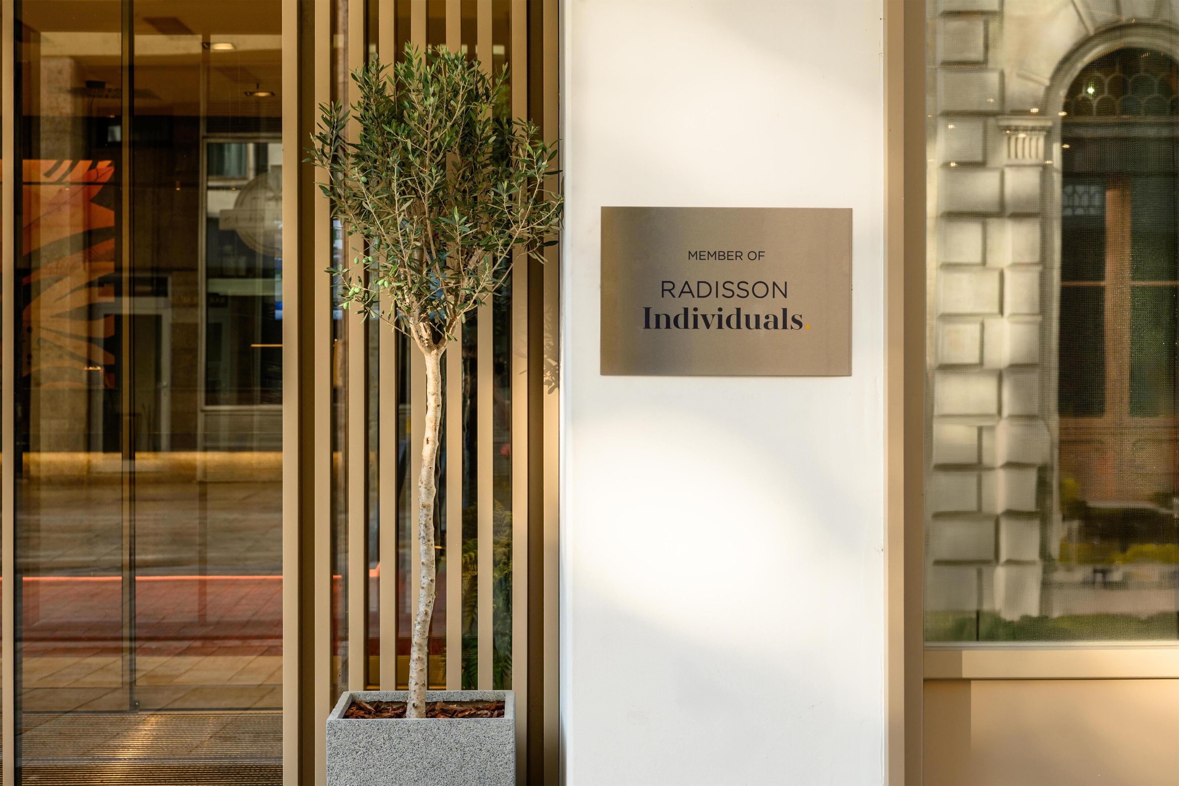 Ein moderner Gebäudeeingang mit einem Schild, das die Mitgliedschaft bei Radisson Individuals kennzeichnet.