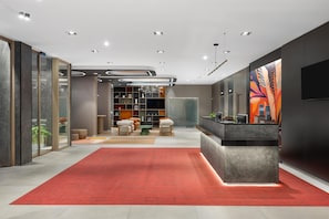 A modern lobby with a red carpet, a reception desk, and a large abstract painting on the wall.