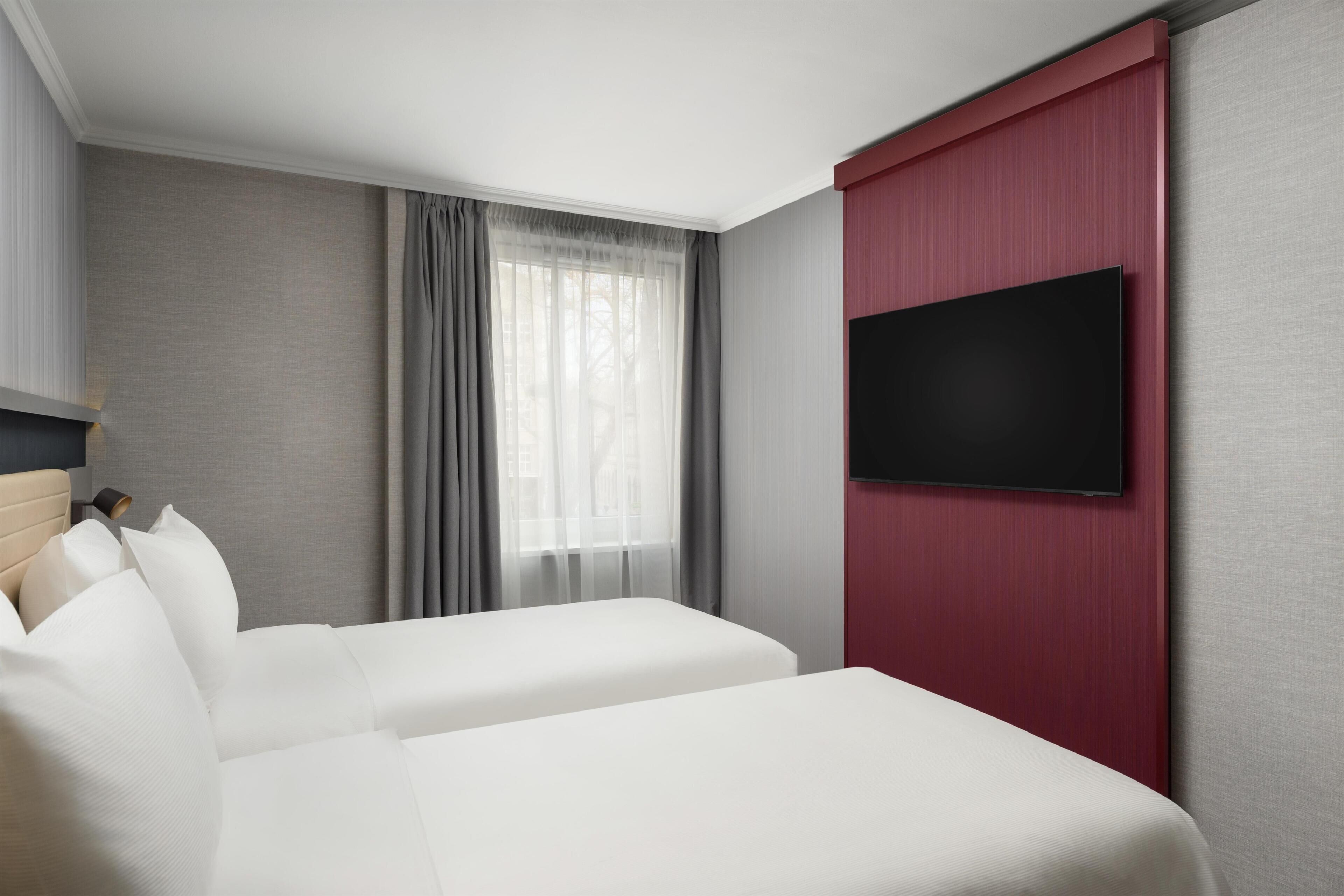 A hotel room with a bed, a TV mounted on the wall, and a window with curtains.
