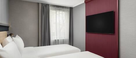 A hotel room with a bed, a TV mounted on the wall, and a window with curtains.