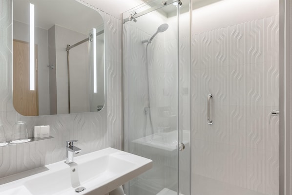Un baño moderno con ducha de vidrio, lavamanos blanco y espejo con marco de madera.